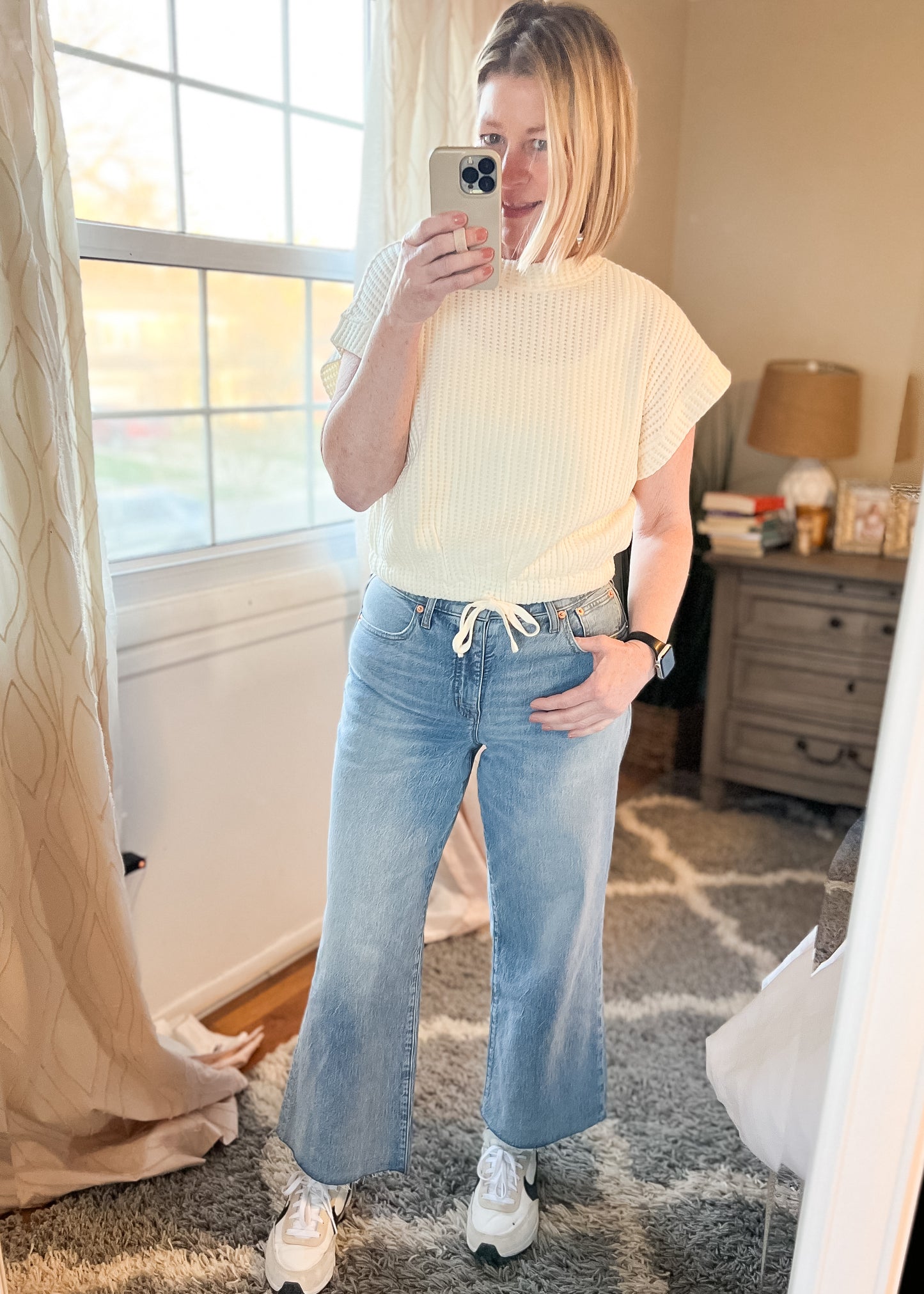 Selfie photo of our Dolman Drawstring Hem Top. Top is a light cream, short sleeves, rounded neckline with a drawstring waist and elastic hemline. Shown with jeans not available in store.