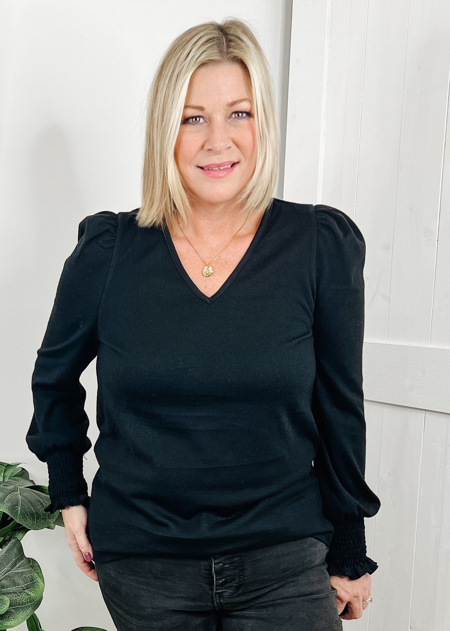 Black v neckline top with puff sleeves and smocked detail around wrists. Top is a heavy knit.