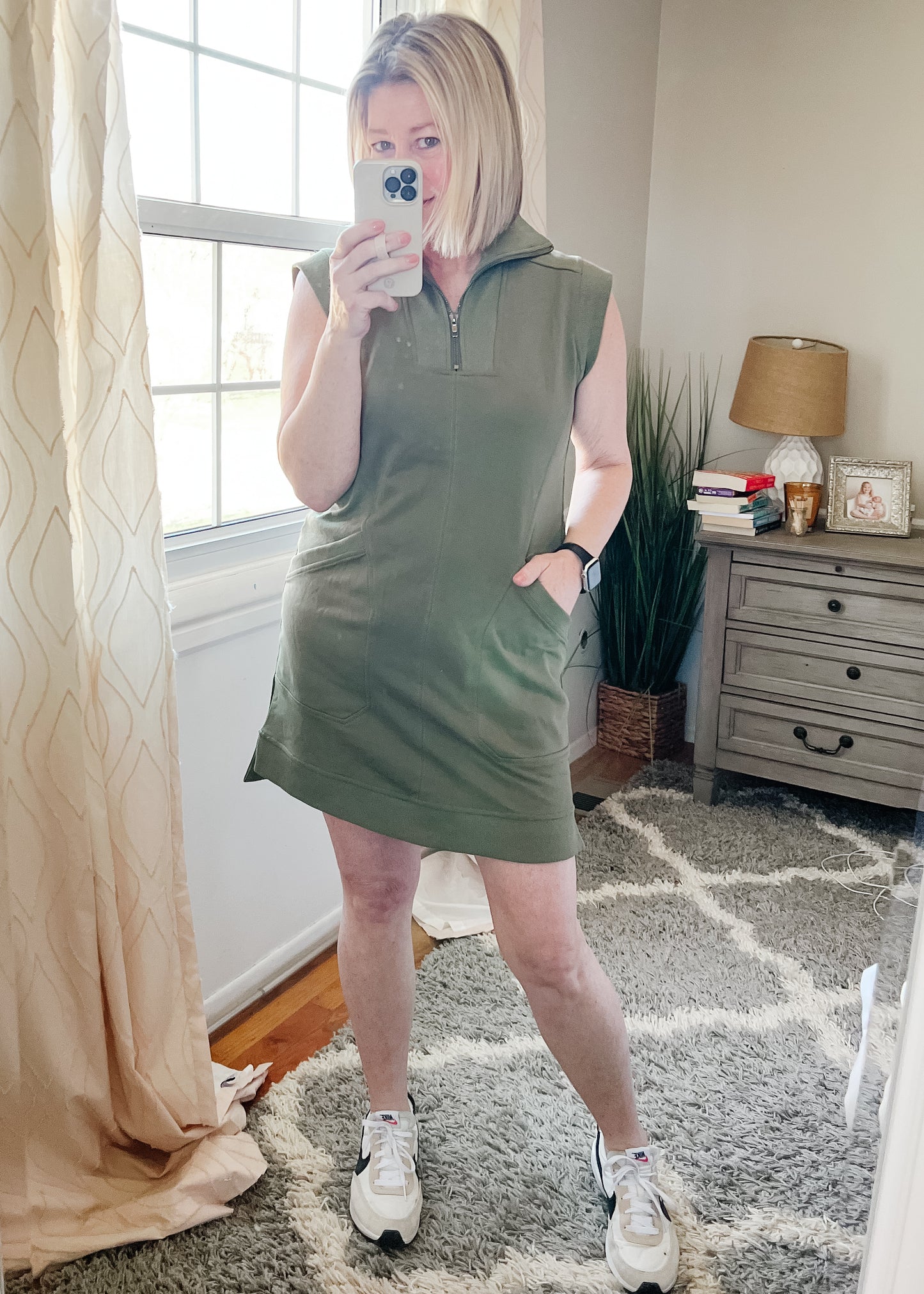 Selfie view of Olive Midi Dress W/Pockets. Dress is a sporty style, has side pockets and is sleeveless. Neckline has high zip collar that can fold over.