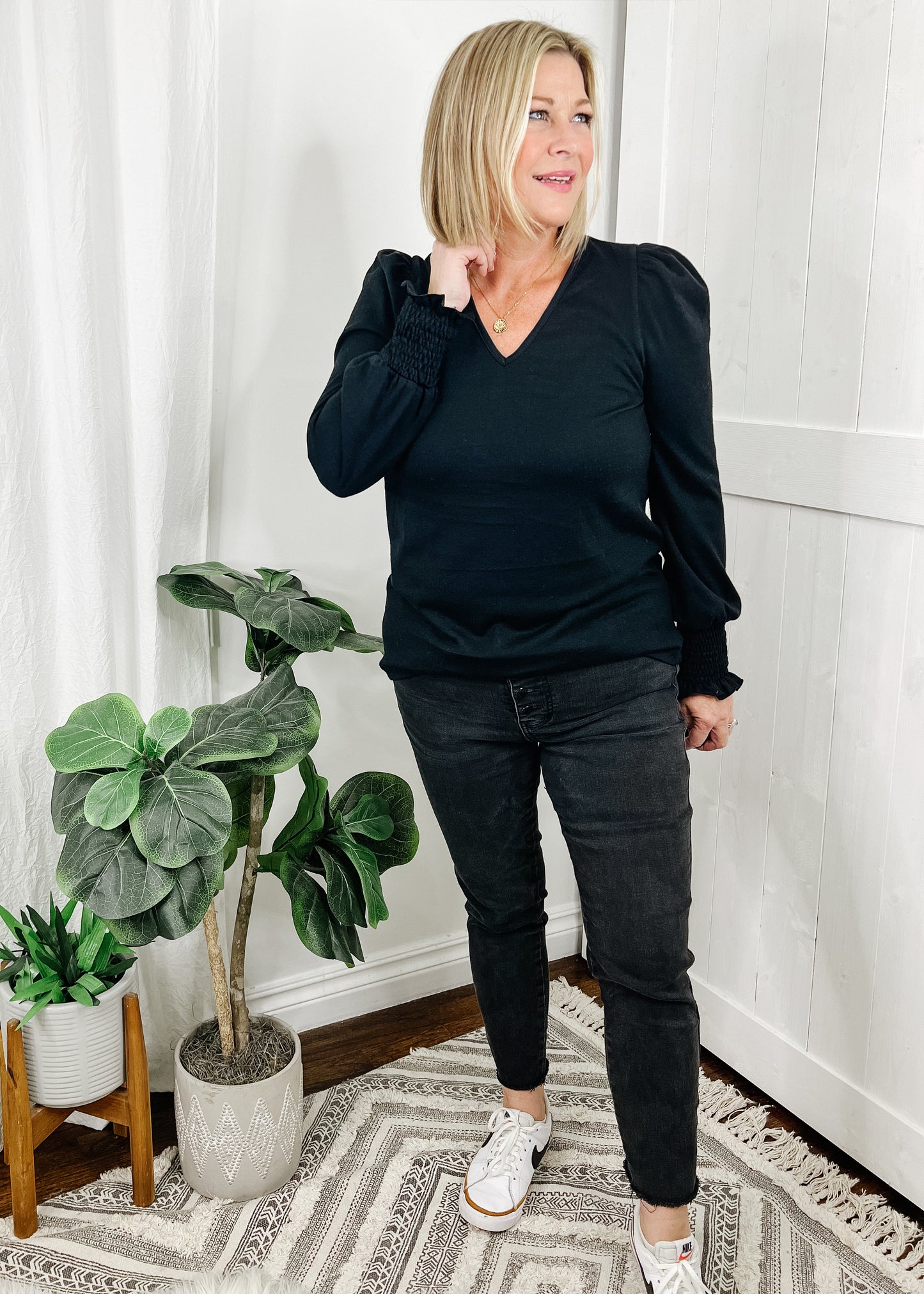 Black v neckline top with puff sleeves and smocked detail around wrists. Top is a heavy knit.