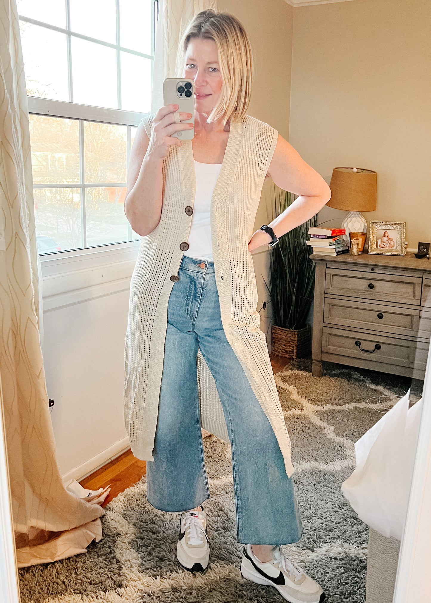 Selfie photo of long open knit sleeveless cardigan in a neutral tan. Cardigan has three button closure.