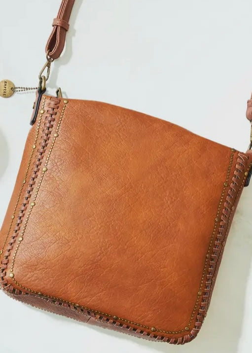 Black vegan leather studded crossbody purse. Purse is 11 x 11 x 4, has gold studded detail around edge, made of a soft vegan leather, top zip closure, back zipper pocket and crossbody strap. Shown in brown.