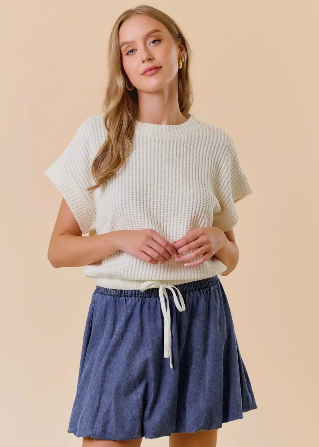 Front model view of our Dolman Drawstring Hem Top. Top is a light cream, short sleeves, rounded neckline with a drawstring waist and elastic hemline. Shown with skirt not available in store.