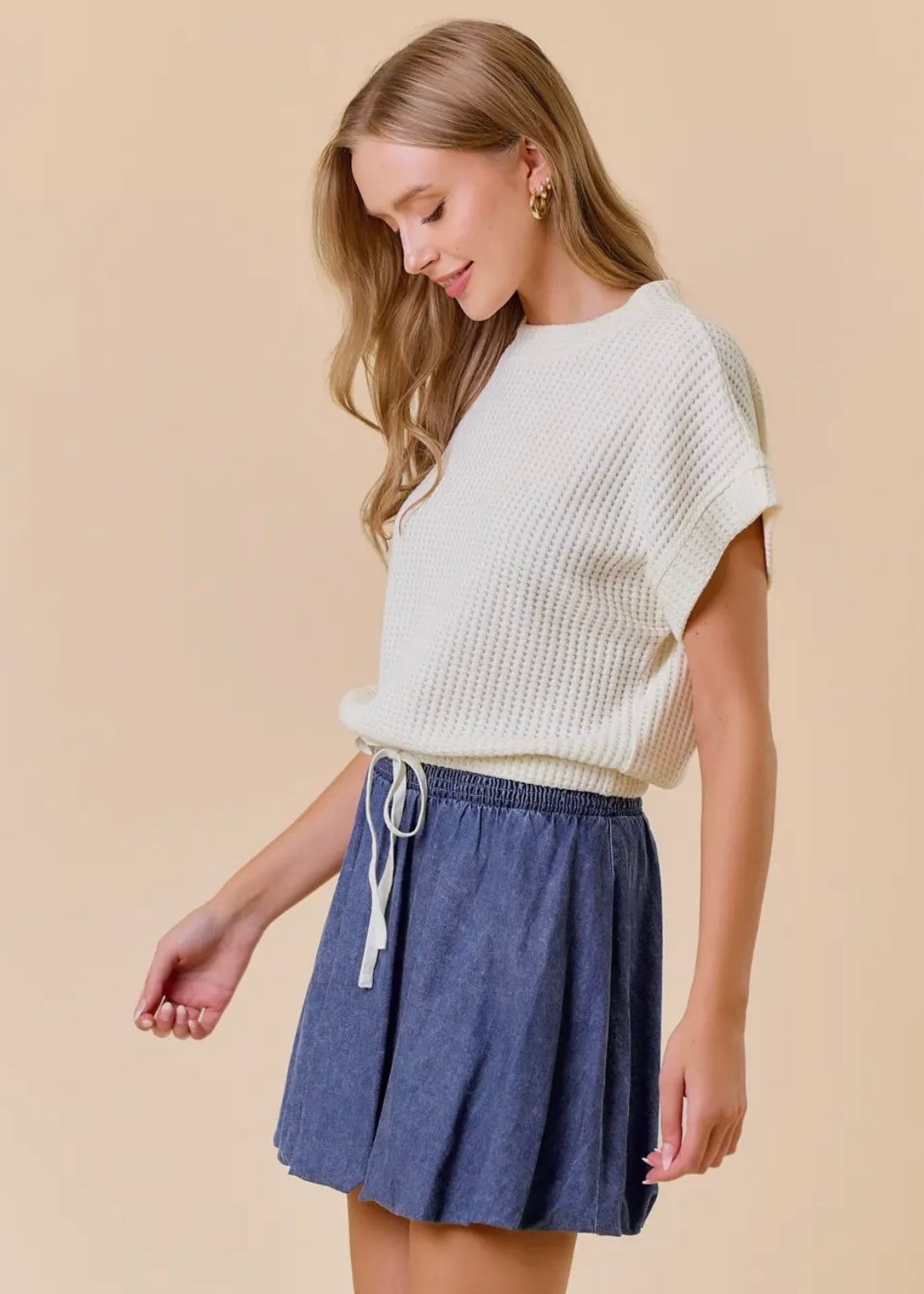 Side model view of our Dolman Drawstring Hem Top. Top is a light cream, short sleeves, rounded neckline with a drawstring waist and elastic hemline. Shown with skirt not available in store.