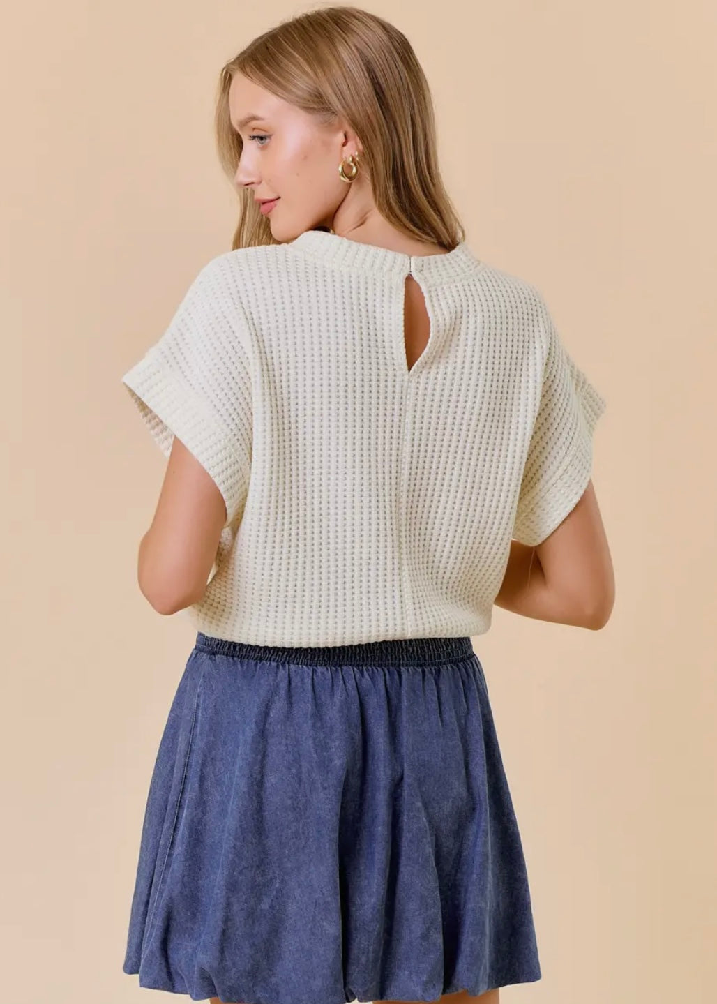 Back model view of our Dolman Drawstring Hem Top. Top is a light cream, short sleeves, rounded neckline with a drawstring waist and elastic hemline. Shown with skirt not available in store.