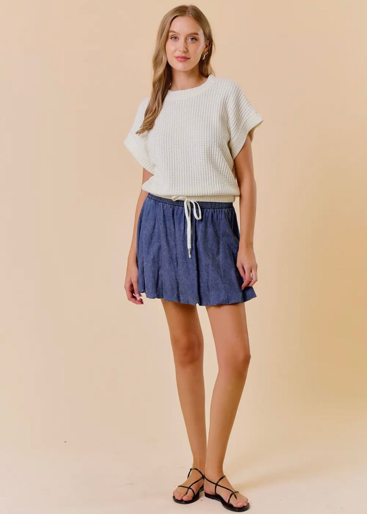 Front full length model view of our Dolman Drawstring Hem Top. Top is a light cream, short sleeves, rounded neckline with a drawstring waist and elastic hemline. Shown with skirt not available in store.