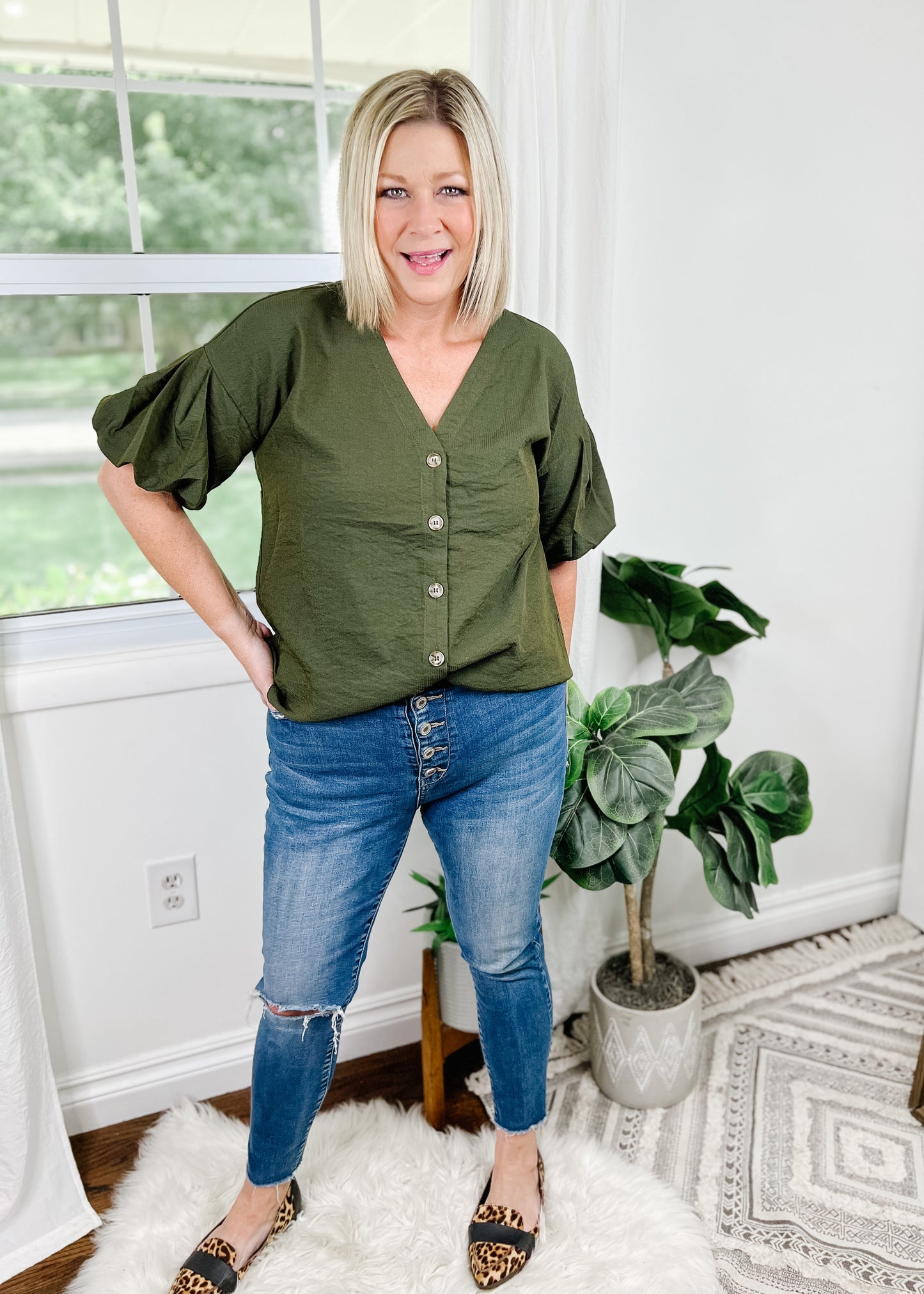 Dark green short sleeve top with bubble sleeves. Top features V-Neckline, buttons up the front and curved hemline.