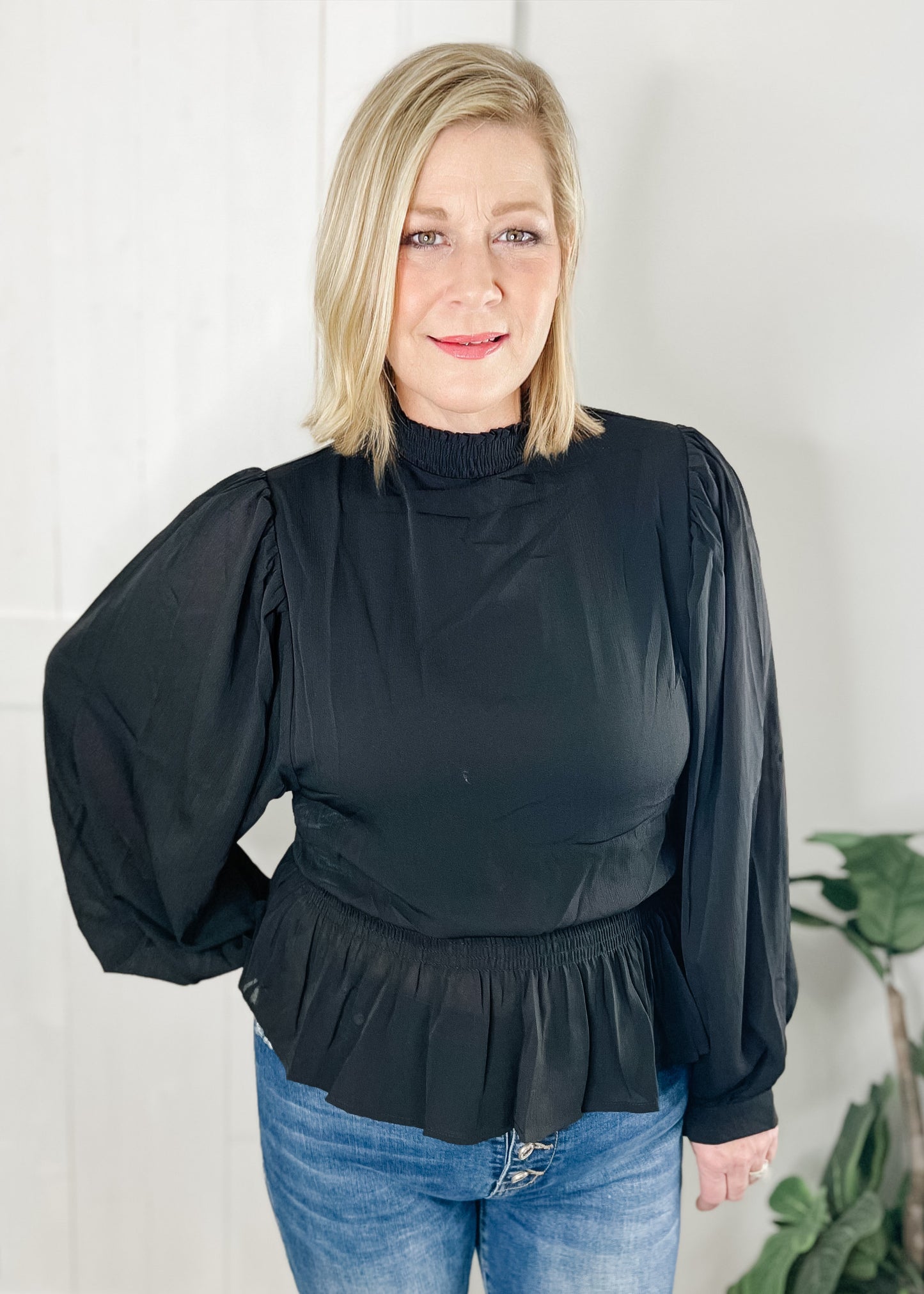 Black peplum blouse with long sleeves double layered bodice with smocked waist with ruffle bottom hemline and smocked mock neck.