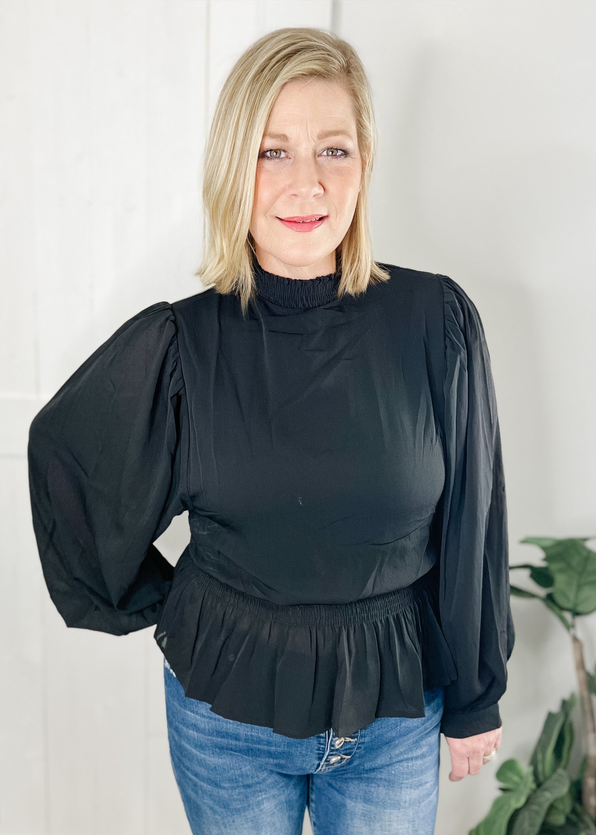 Black peplum blouse with long sleeves double layered bodice with smocked waist with ruffle bottom hemline and smocked mock neck.