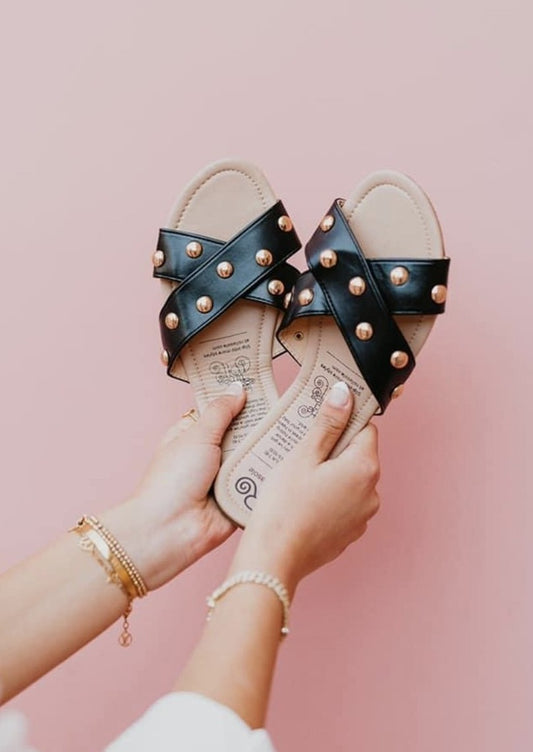 Black flexible slip on sandals with cross cross design and gold studs.