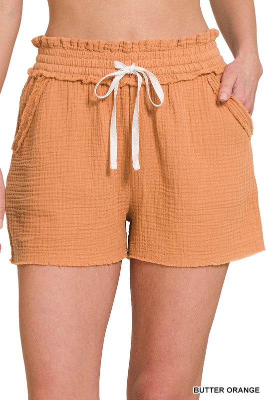 Drawstring shorts in a light muslin fabric with functional drawstrings. Features pockets and elastic waist. Shown in orange. 