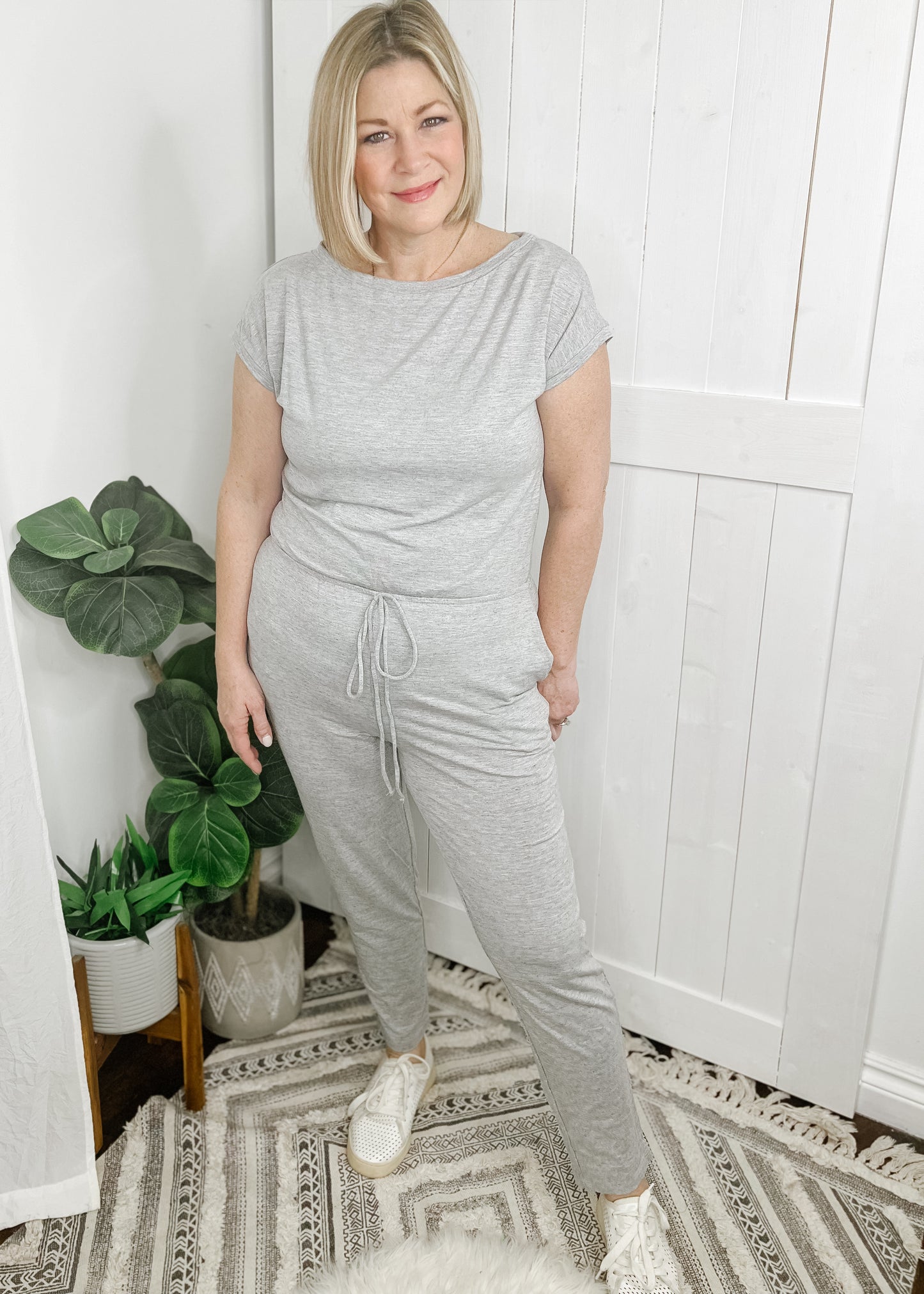 Gray jumpsuit with boat neckline, short sleeves and tapered legs. Jumpsuit has side pockets and elastic waist with faux drawstring. 