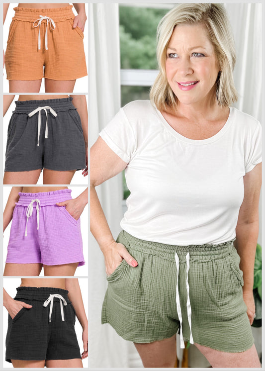 Drawstring shorts in a light muslin fabric with functional drawstrings. Features pockets and elastic waist. Shown in, olive, orange, charcoal, lavender and black.