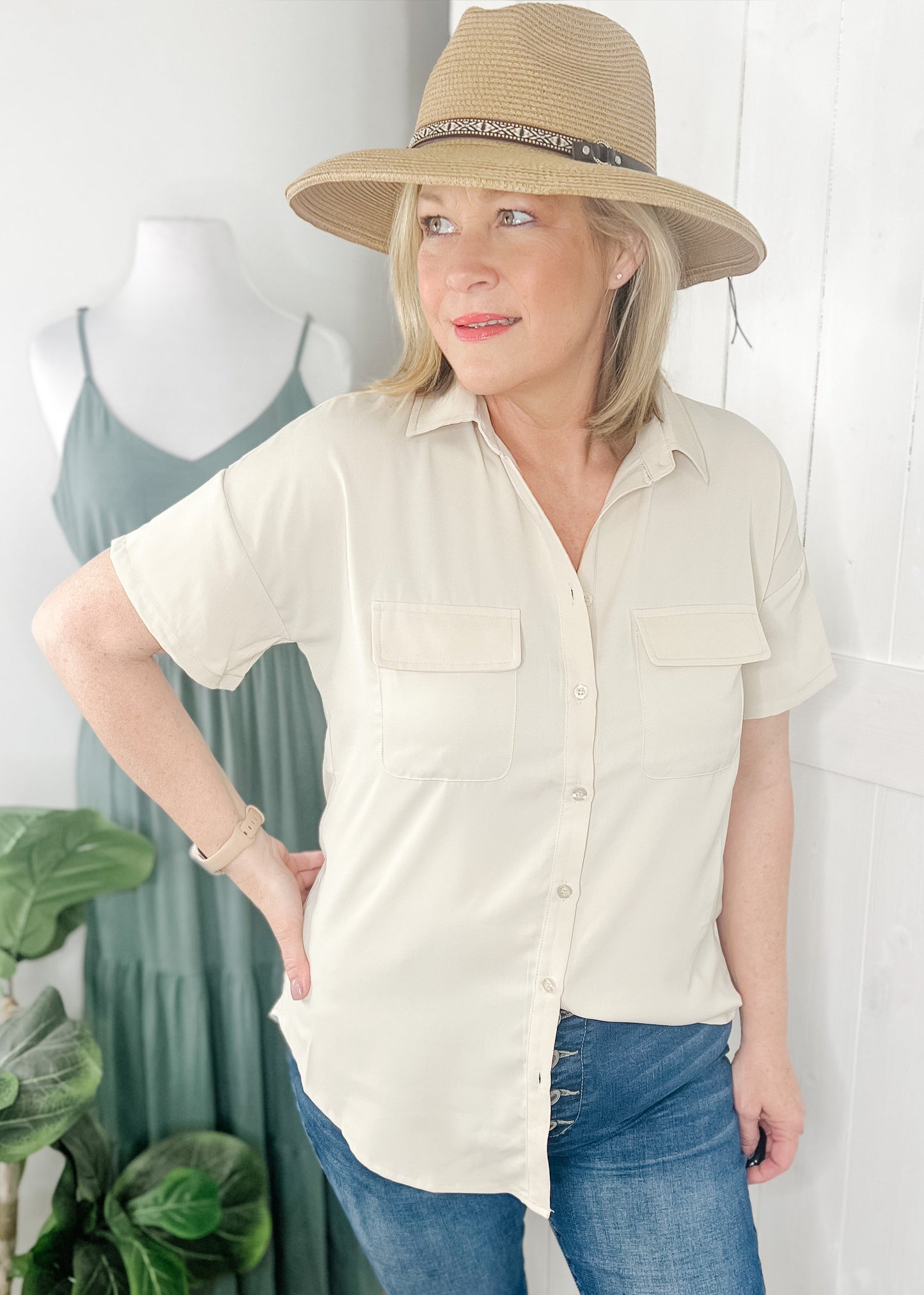 Classic short sleeve button up in a. soft beige with collar, flap chest pockets and rounded hemline. Shown with out high rise skinny jeans and Carolina sun hat.
