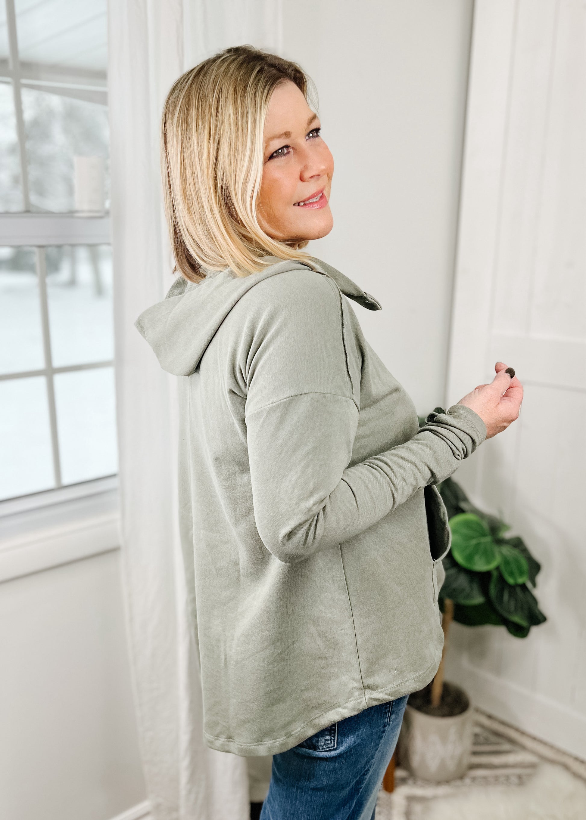 Sage green hoodie top with functional collar buttons opening hoodie. Top also features a kangaroo pocket in the front, slender long sleeves and flare bodice the gradually gets longer in the back. 