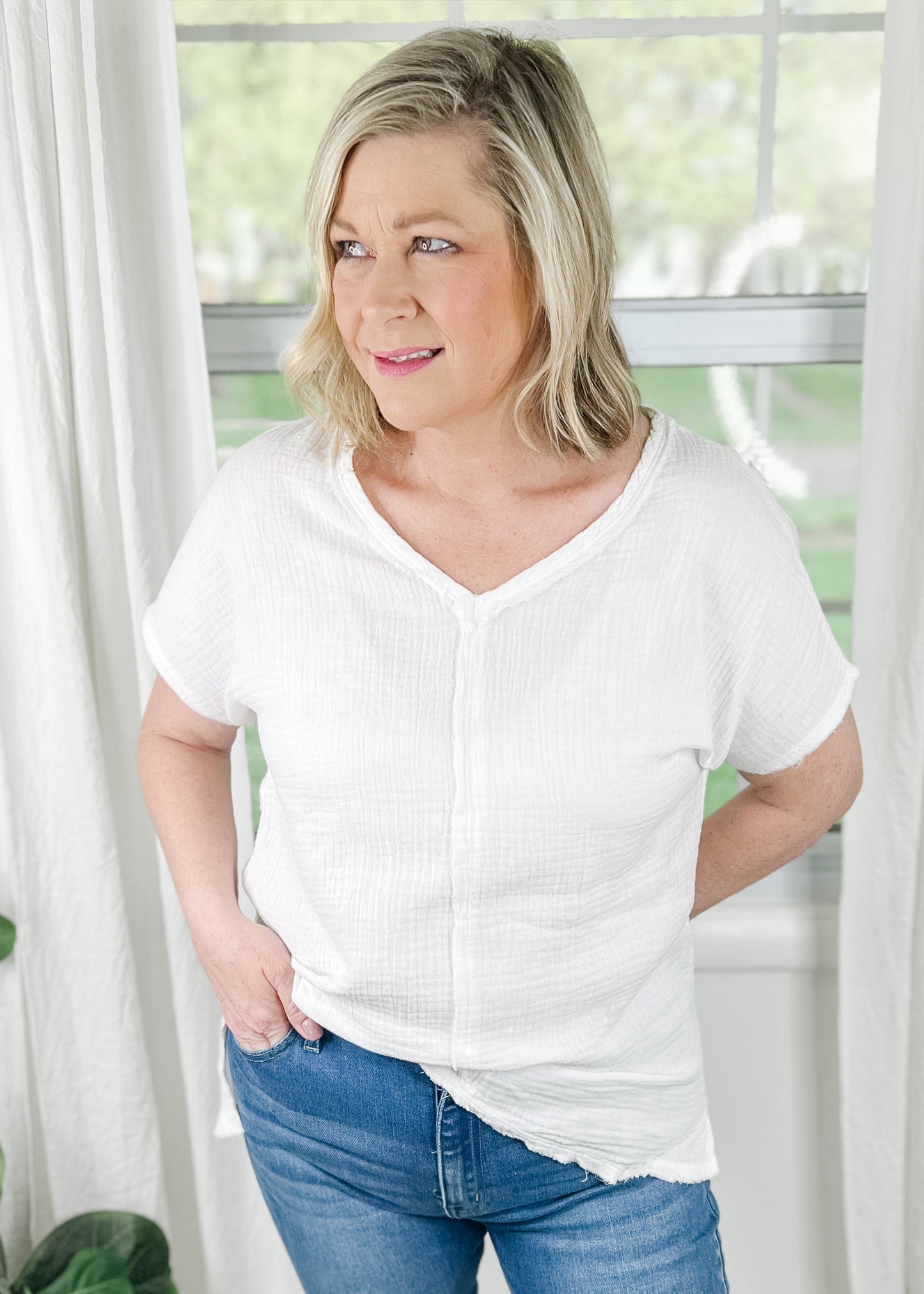White V neck top in a soft muslin fabric and raw hemlines. Short sleeves, Side slits and hi low hemline. Top features reversed stitching down the front and back center. 