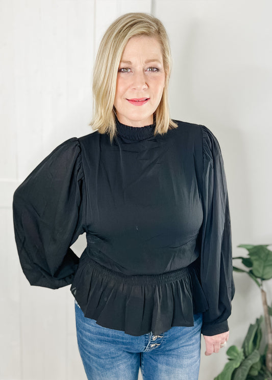 Black peplum blouse with long sleeves double layered bodice with smocked waist with ruffle bottom hemline and smocked mock neck.