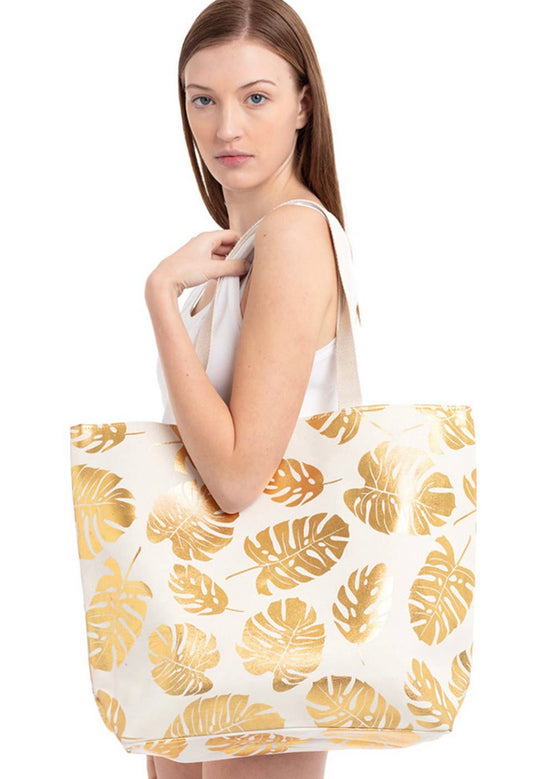 Cream beach bag with gold foil tropical leaves imprinted  throughout.  Bag has a snap closure and long straps. 